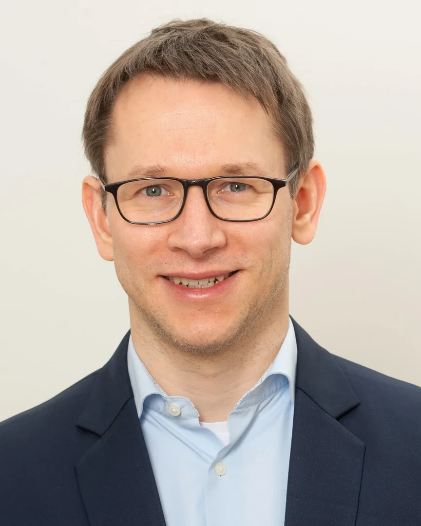 Eine Wissenschaftlerin und ein Wissenschaftler arbeiten hinter einer Glasfassade und mischen Chemikalien mit Großgeräten.