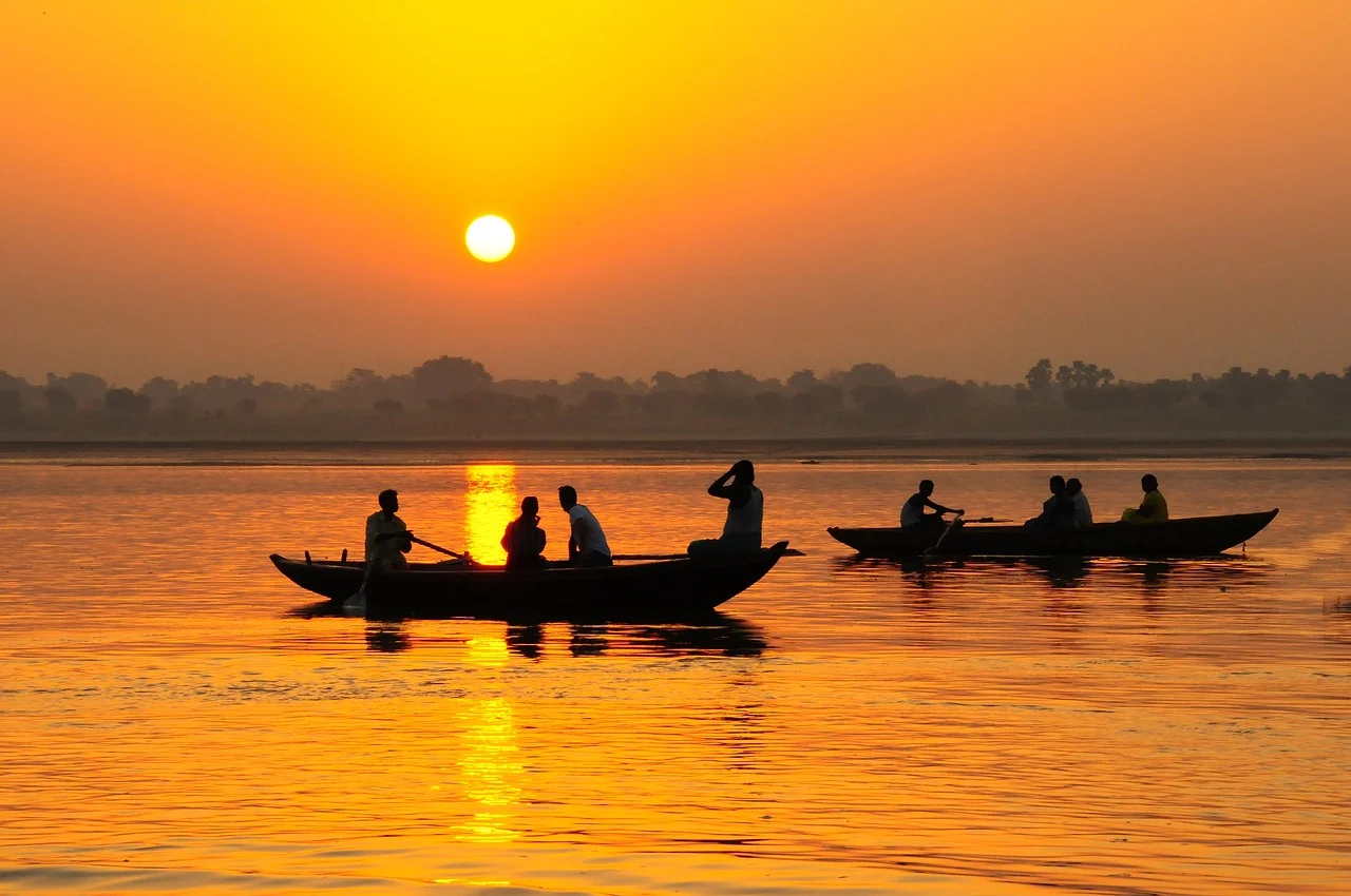 Bright orange sunset over a body of water with two small boats carrying a few people.