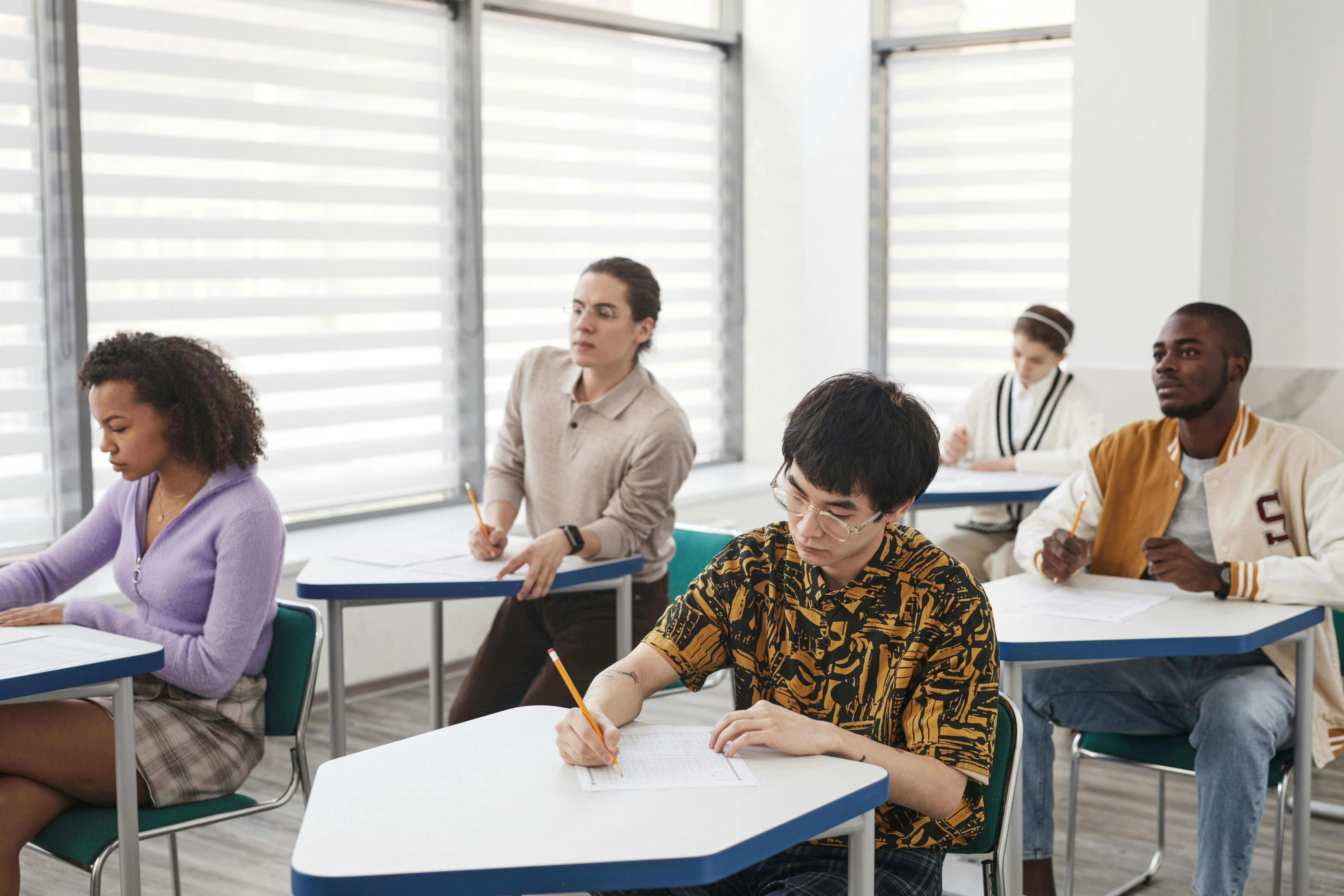 Five students writing in a bright classroom.